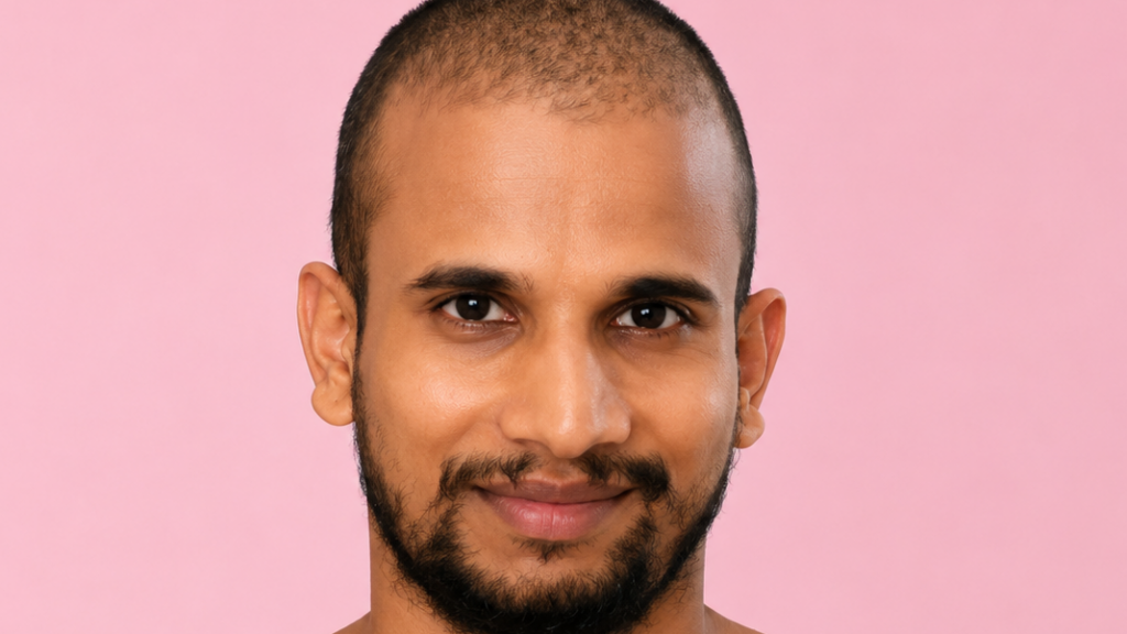 Close-up portrait of a smiling man with a short haircut and beard against a pink background.
