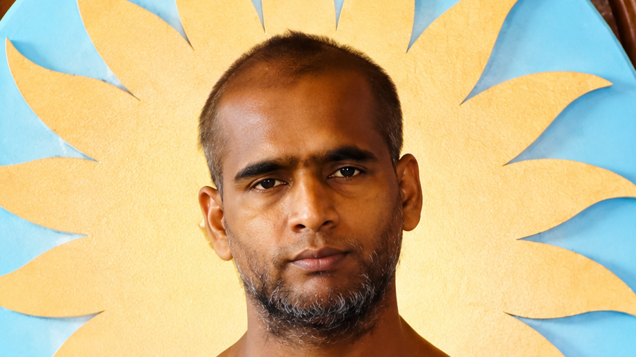 Close-up portrait of a man with short hair and gray stubble in front of a large yellow sunburst on a blue background.