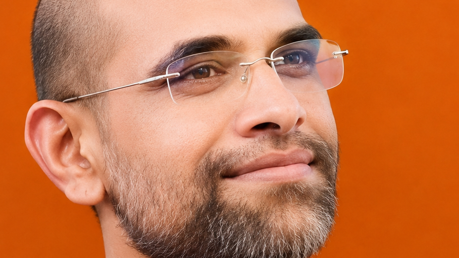 Close-up of a bearded man wearing rimless glasses, looking upward, with an orange background.