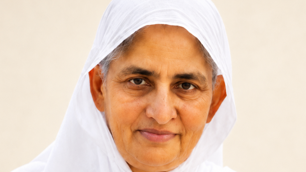 Close-up of a smiling woman wearing a white headscarf against a neutral background.