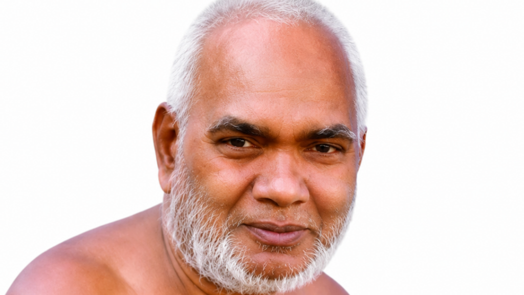 Close-up portrait of an older man with a white beard, looking at the camera against a plain white background.