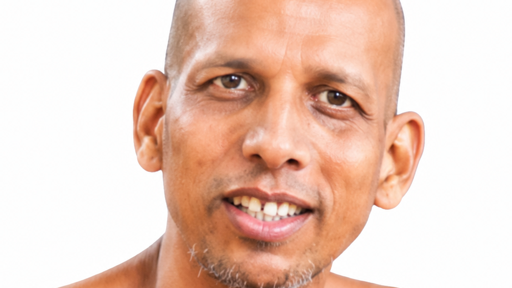 Close-up portrait of a smiling man with a shaved head and light facial hair against a white background.