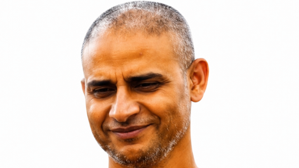 Close-up portrait of a smiling man with short gray stubble against a white background, looking slightly downward.