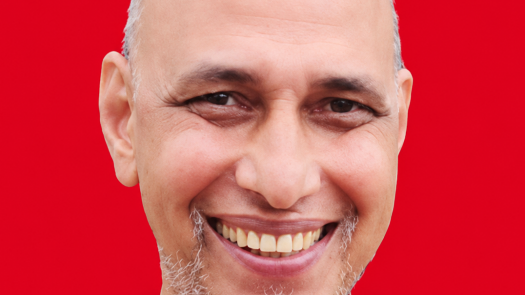 Close-up portrait of a smiling man with a gray goatee against a solid red background, conveying friendliness.