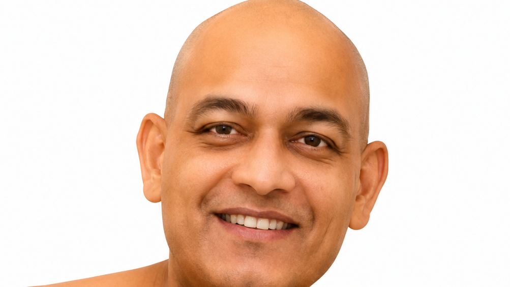 Close-up portrait of a smiling man with a shaved head against a white background.