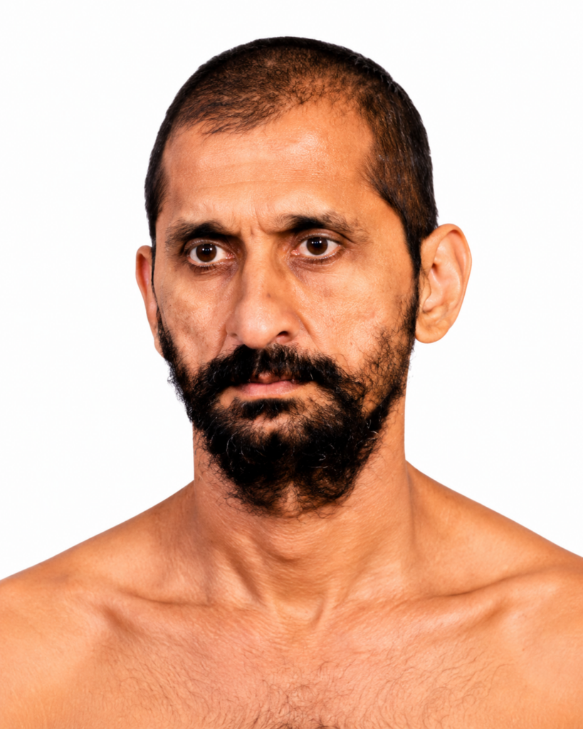 Head-and-shoulders portrait of a man with dark hair and beard, looking intently at the camera against a white background, bare shoulders visible.