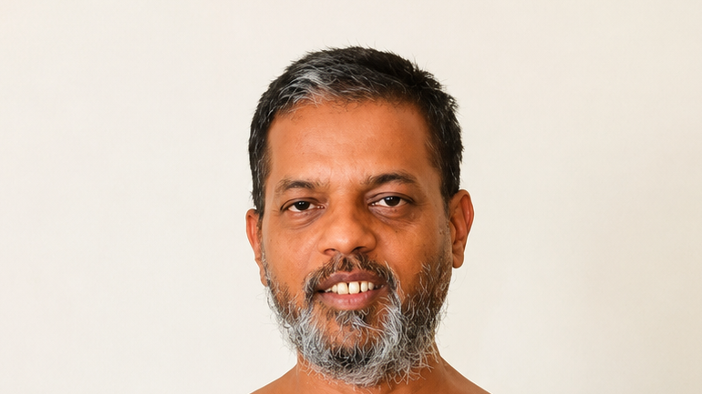 Close-up portrait of a middle-aged man with short black and gray hair and a graying beard, smiling at the camera against a light background.