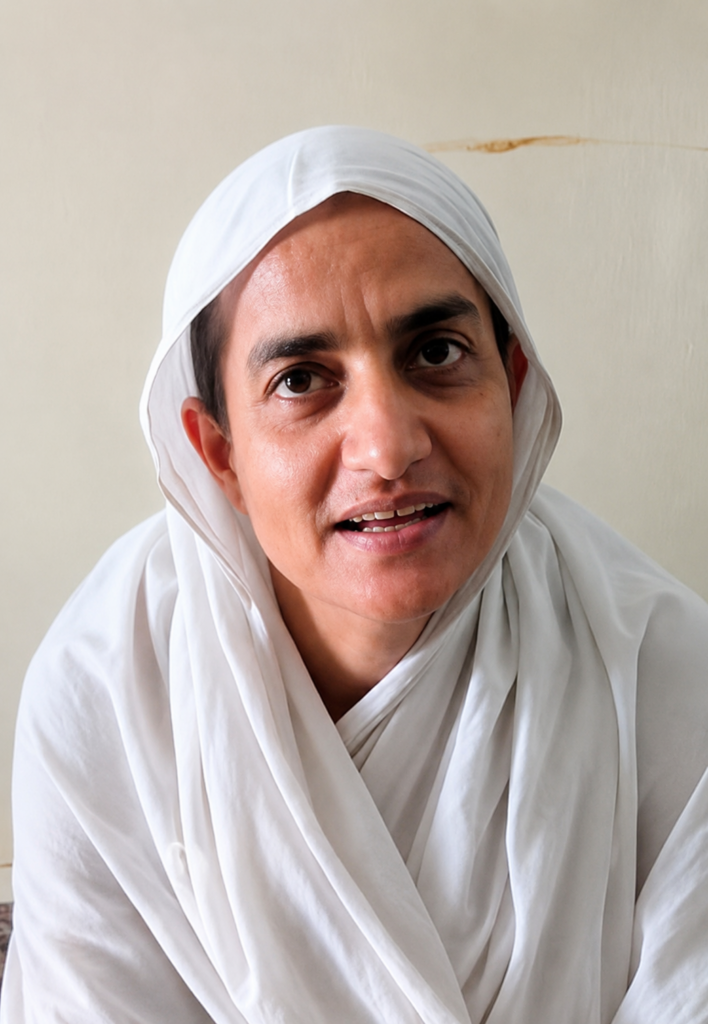 Person in a white hijab and robe looking at the camera against a light wall.