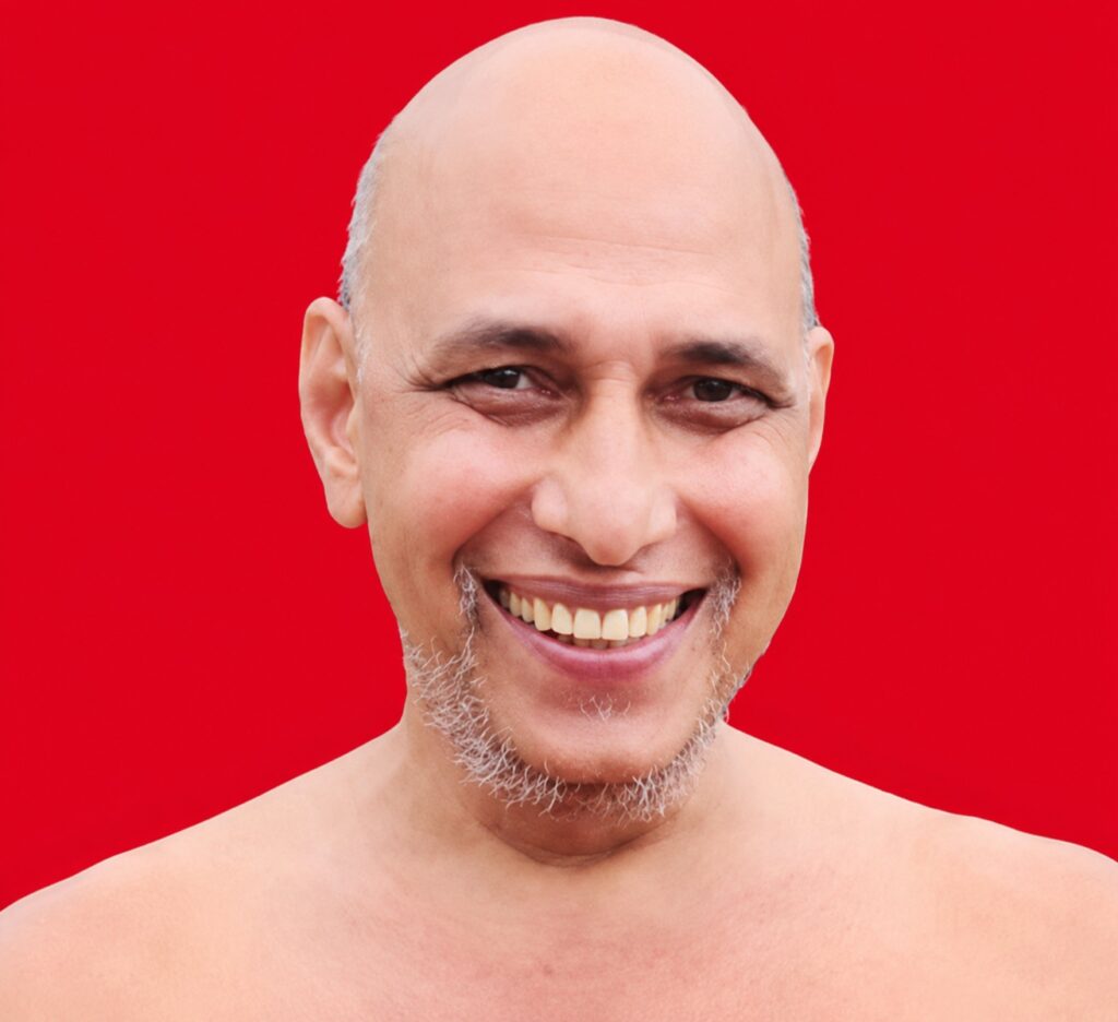Smiling bald man with a gray beard against a solid red background, shoulders visible.