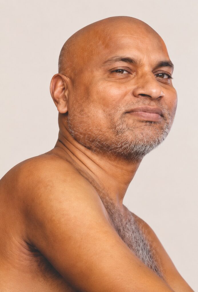 Close-up portrait of a bald man with a gray stubble beard looking slightly to the right against a neutral background.