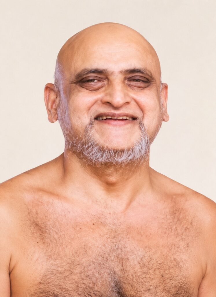 Smiling bald man with a gray beard and chest hair, facing the camera against a beige background.