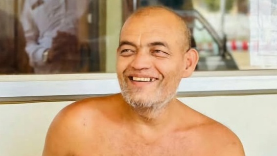 Smiling shirtless middle-aged man with a gray beard indoors, looking off to the side.