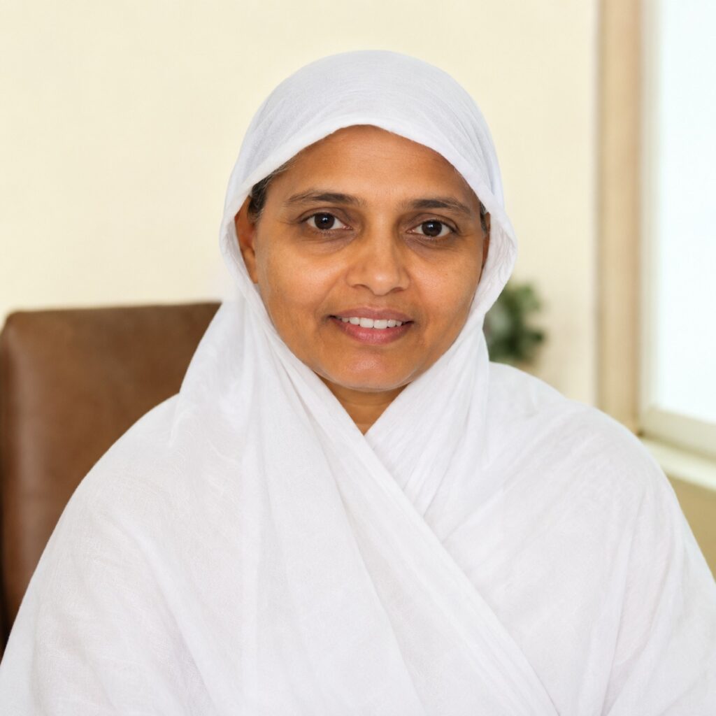 Smiling woman in a white hijab and robe, seated indoors.