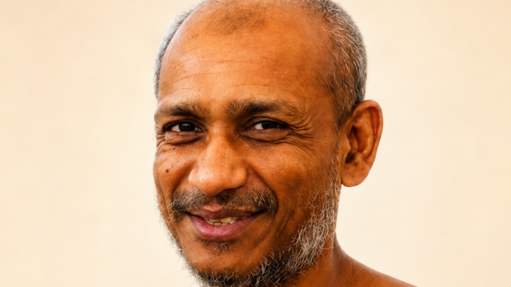 Close-up portrait of a smiling middle-aged man with a gray beard against a beige background.
