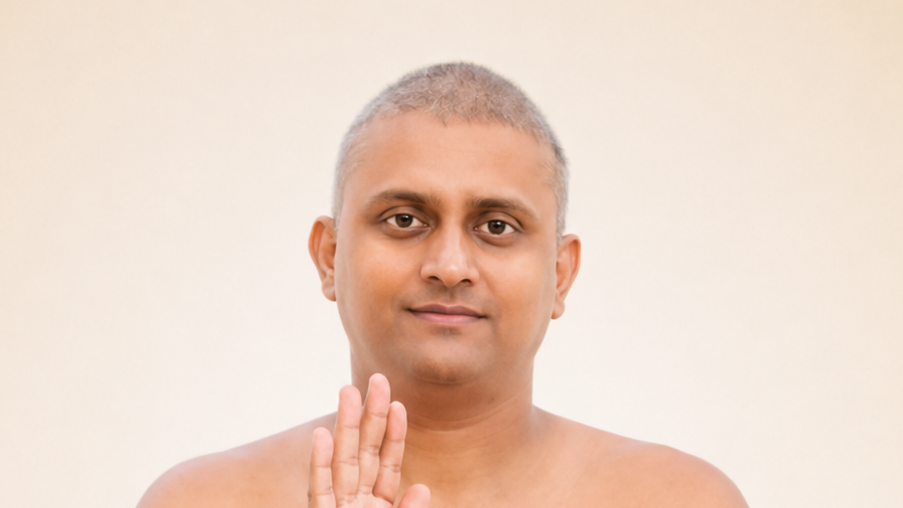 Portrait of a man with short gray hair facing the camera, right hand raised in a blessing gesture with an open palm.