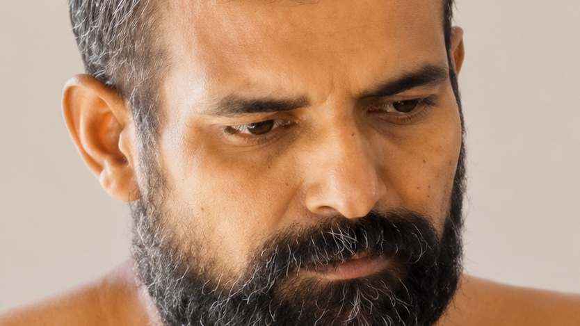 Close-up of a bearded man looking down with a thoughtful or serious expression.
