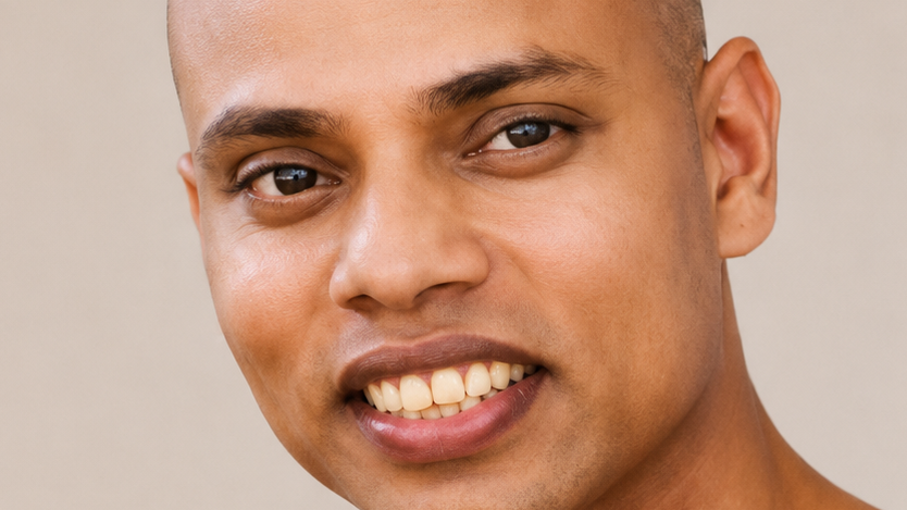Close-up of a smiling man showing teeth, cropped headshot against a neutral background
