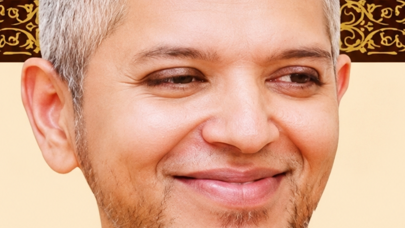 Close-up of a smiling man with short gray-streaked hair and light stubble against a warm beige background.