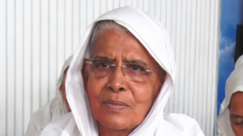 Portrait of an elderly woman in a white headscarf and glasses, looking ahead with a calm expression.