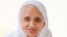 Portrait of an elderly woman wearing a white headscarf, smiling at the camera.