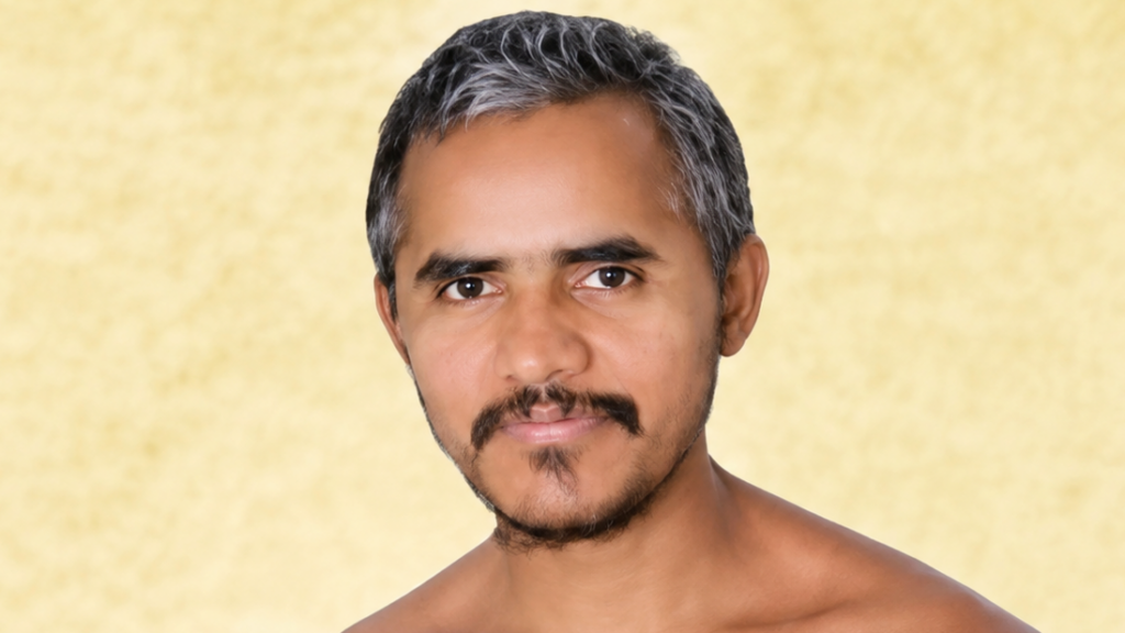 Portrait of a man with short gray-streaked hair and a mustache against a pale yellow patterned background.