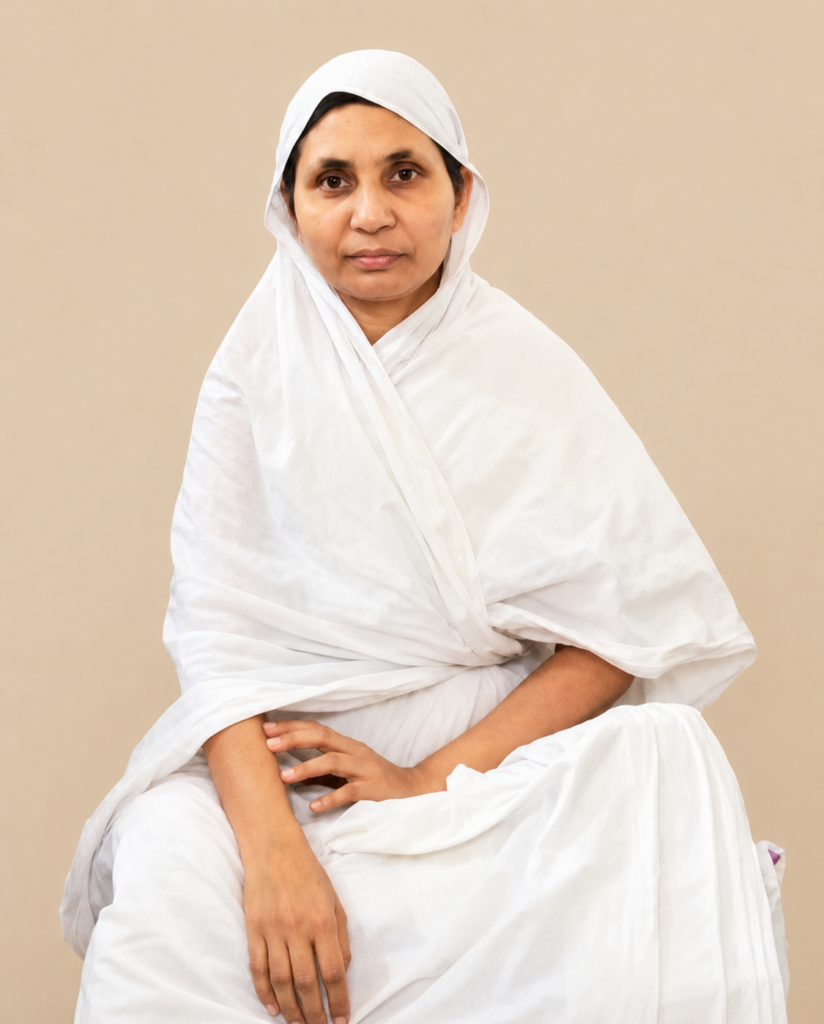 Woman in a white traditional outfit seated against a beige background, looking at the camera.