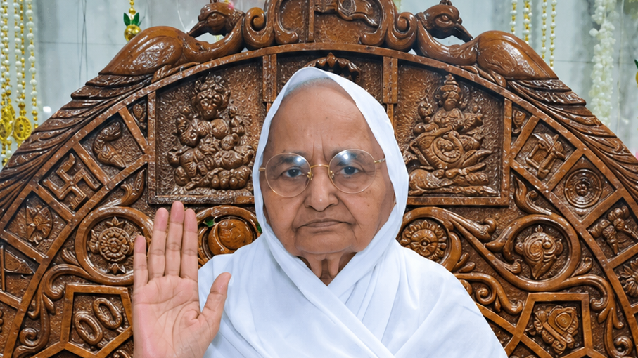 Old woman in a white headscarf and glasses sits before an ornately carved wooden backdrop, raising her right hand in a blessing gesture.