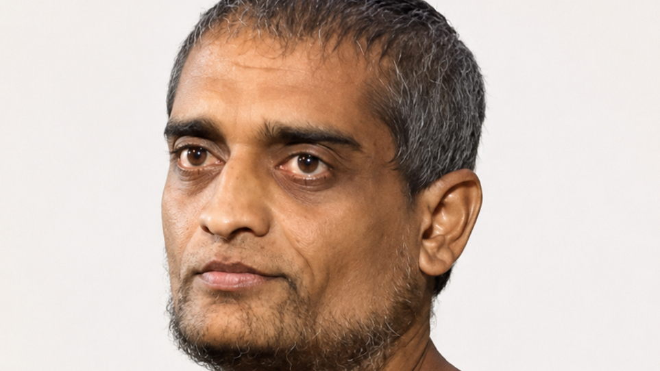 Close-up portrait of a middle-aged man with short gray-streaked hair and stubble, facing slightly left, neutral expression.