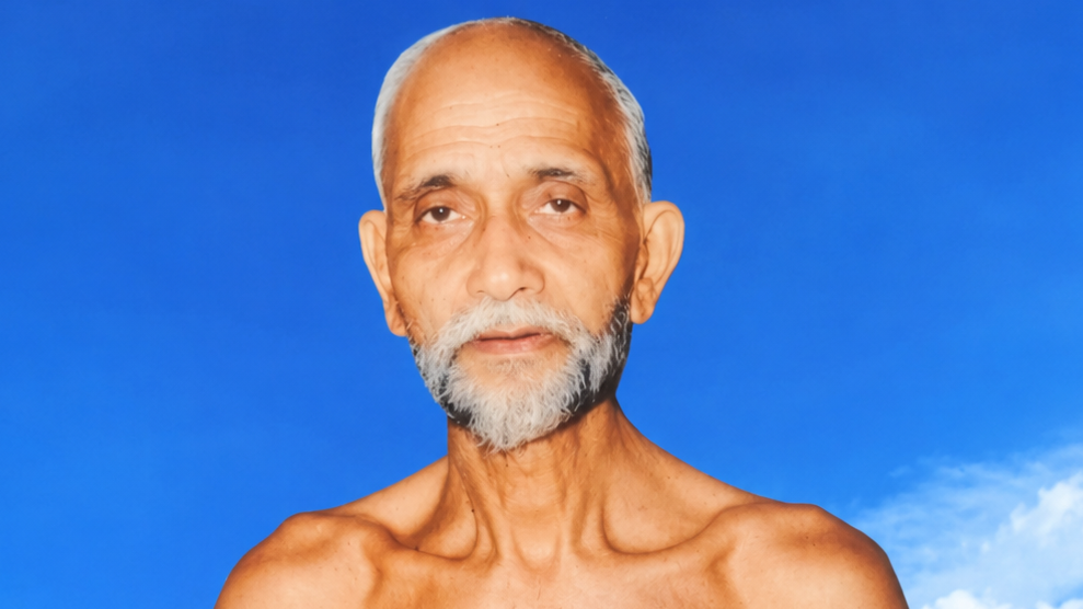 Older man with a gray beard, shirtless, against a bright blue sky backdrop.