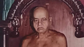 Shirtless, stern-looking older man seated on an ornate carved wooden throne.
