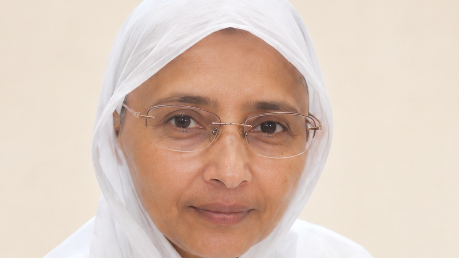 Close-up portrait of a woman wearing a white headscarf and glasses, looking at the camera with a gentle smile.