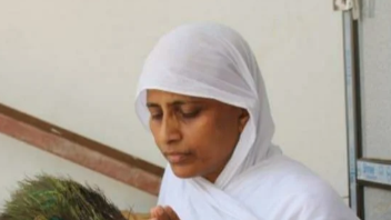 Woman in a white headscarf and robe looking down at a plant.