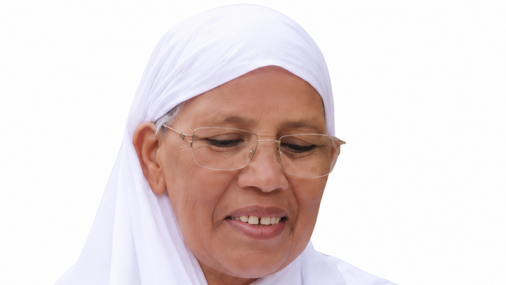 Close-up of an elderly woman wearing a white hijab and glasses, looking down with a gentle smile.
