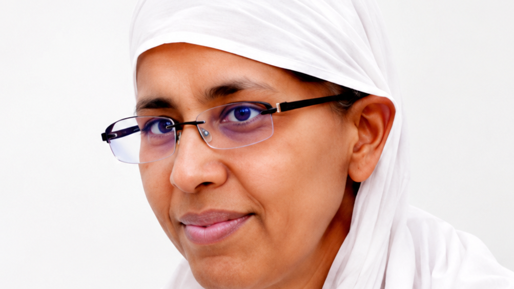 Close-up of a woman wearing a white hijab and glasses, looking at the camera with a gentle smile.