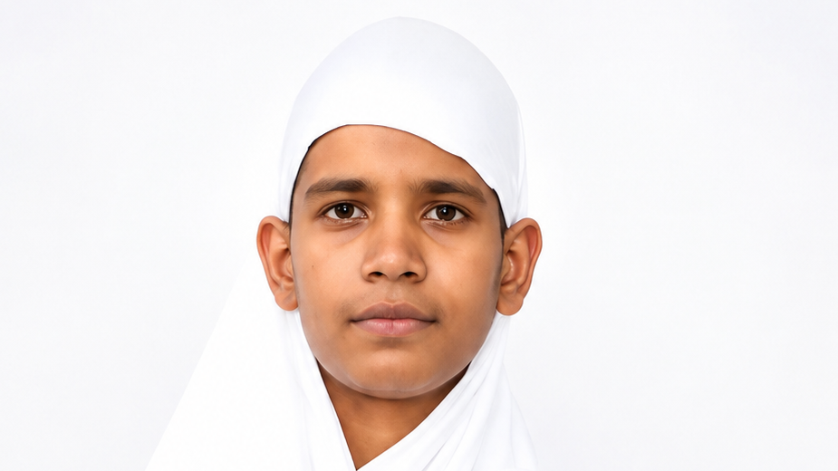 Close-up portrait of a young boy wearing a white hijab against a light background, facing the camera.