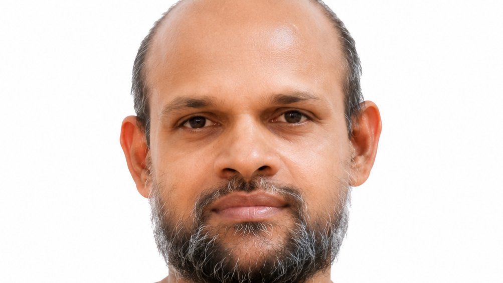 Close-up portrait of a man with a trimmed gray beard looking at the camera against a white background with a neutral expression.