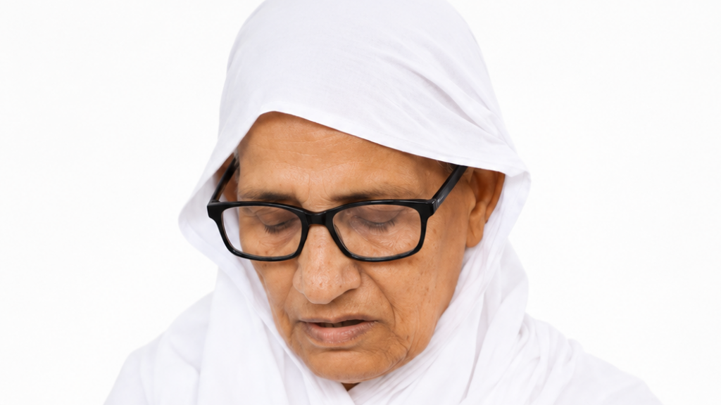 Elderly person wearing a white headscarf and black rectangular glasses, looking down.