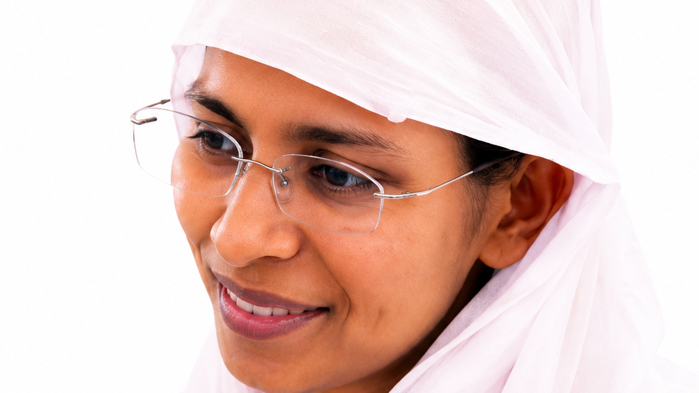 Close-up of a smiling woman wearing a pale pink hijab and clear-framed glasses.