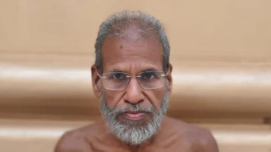 Man with gray beard and glasses looking directly at the camera against a beige background, bare shoulders visible.