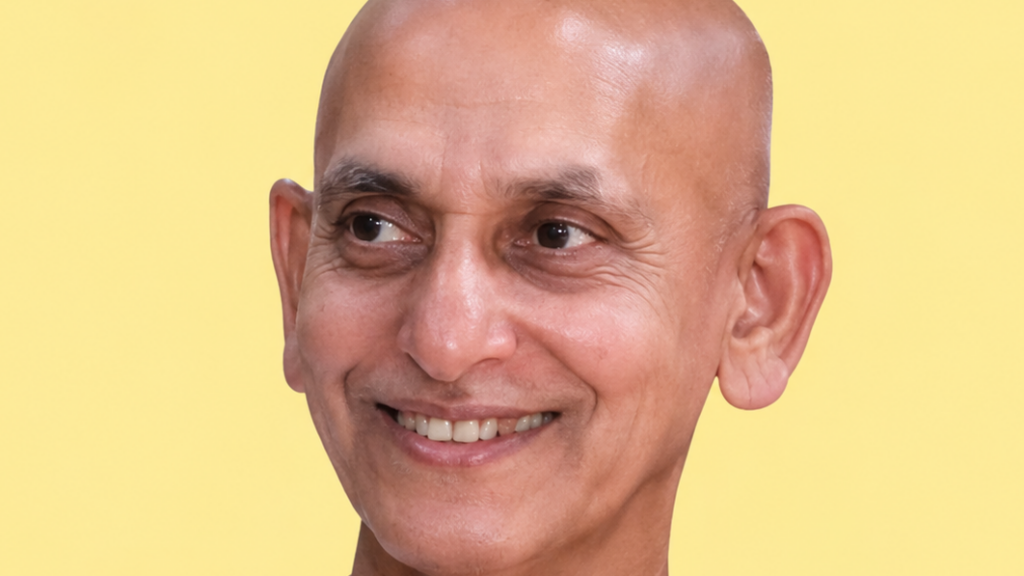 Close-up portrait of a smiling bald man against a pale yellow background.