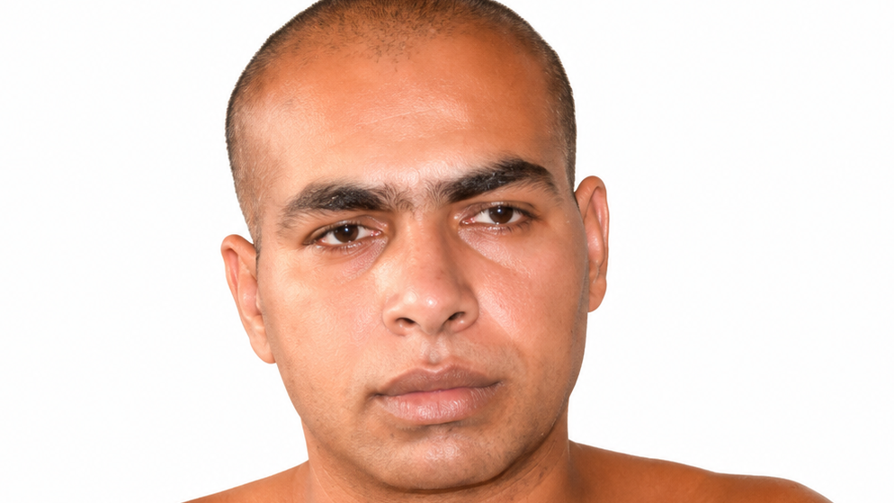 Close-up portrait of a man with a shaved head and a neutral expression against a white background.