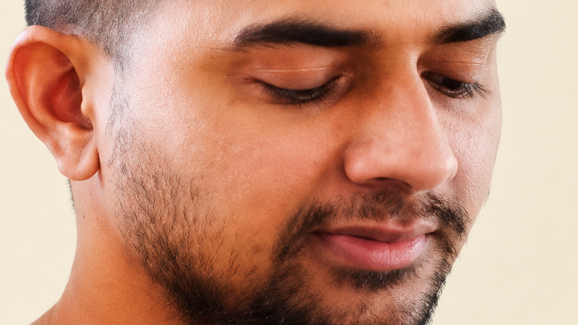 Close-up of a man with a trimmed beard and short hair, eyes closed, serene expression.