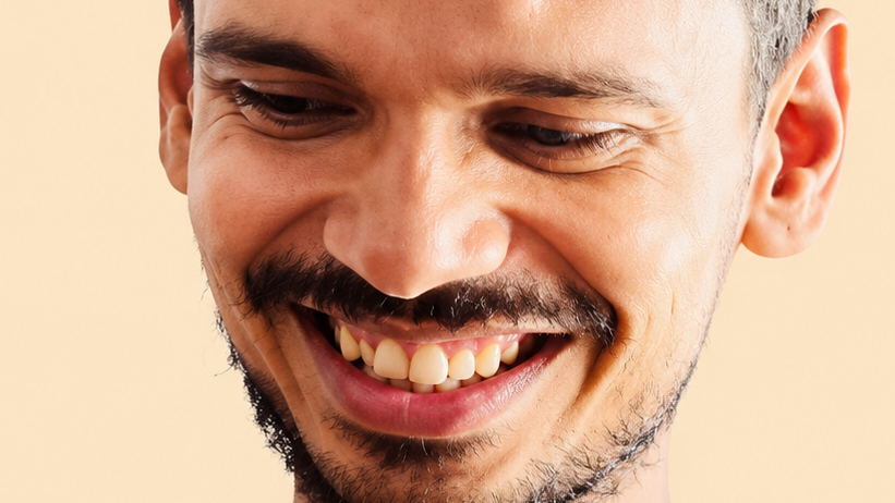 Close-up of a man smiling, showing teeth and light stubble on his face.