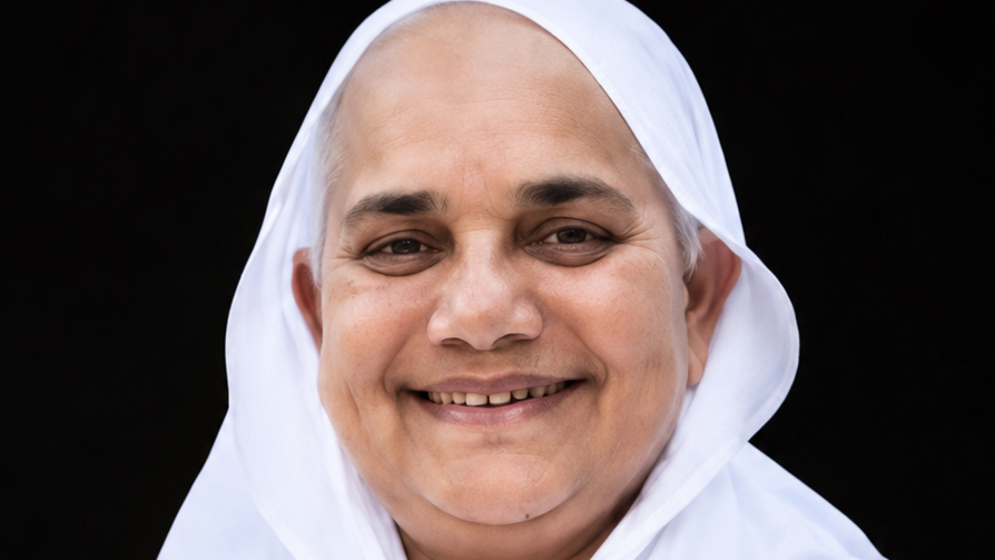 Close-up of a smiling woman wearing a white headscarf against a dark background.