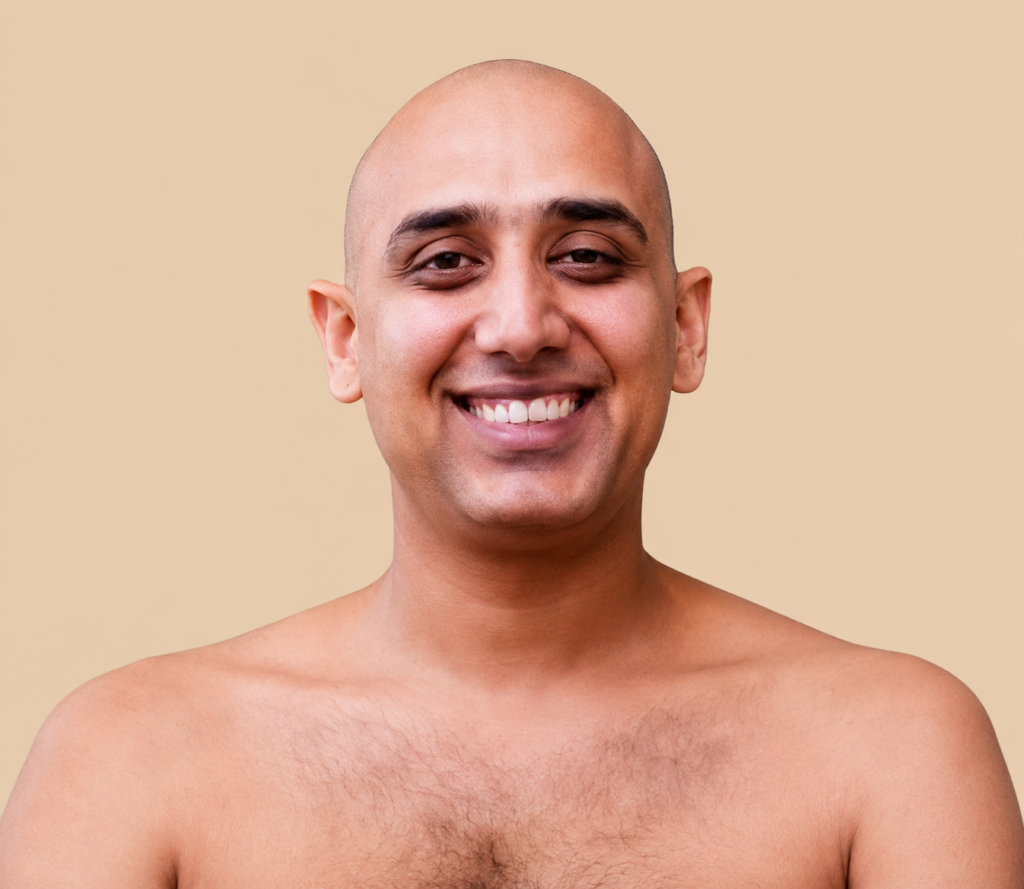 Smiling bald man facing the camera with bare shoulders against a beige background.
