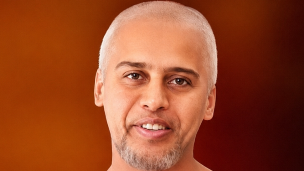 Portrait of a smiling man with short gray hair and a light goatee against an orange-brown gradient background.