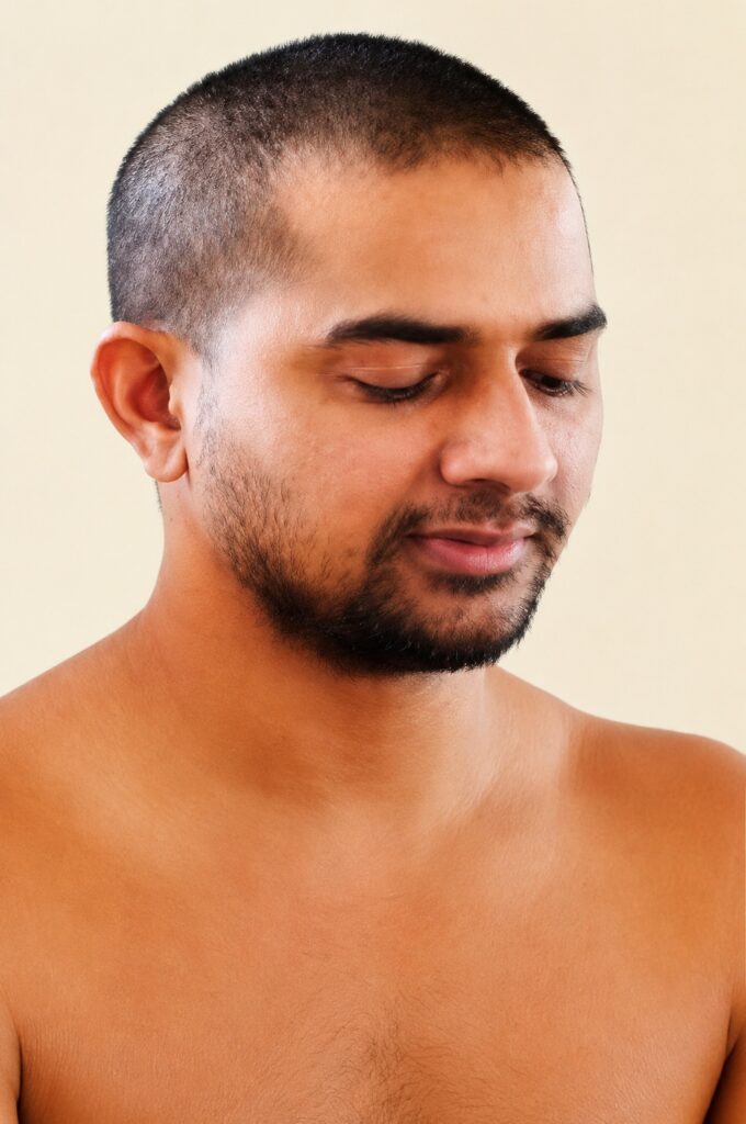 Close-up portrait of a man with a short buzz cut and trimmed beard, looking downward.