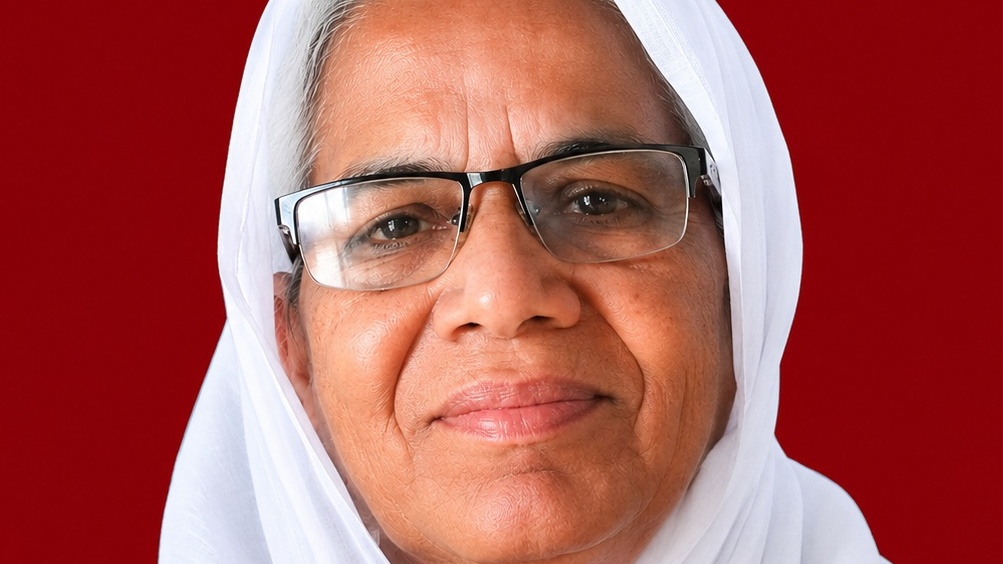 Close-up of a smiling woman wearing a white headscarf and glasses against a red background.