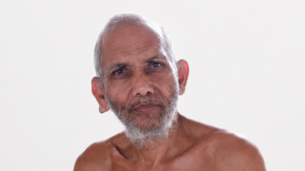 Close-up portrait of an older man with a white-gray beard, looking slightly to the side against a light background.