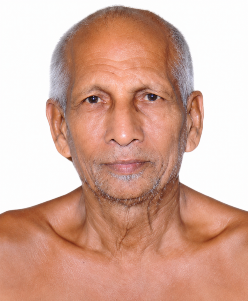 Close-up portrait of an elderly man with short gray hair and stubble against a white background.